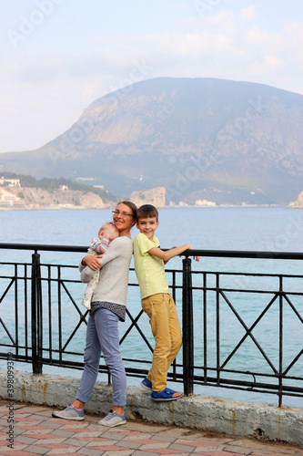 Happy tourist family, mother and two sons, big and small, look at the Black Sea from promenade