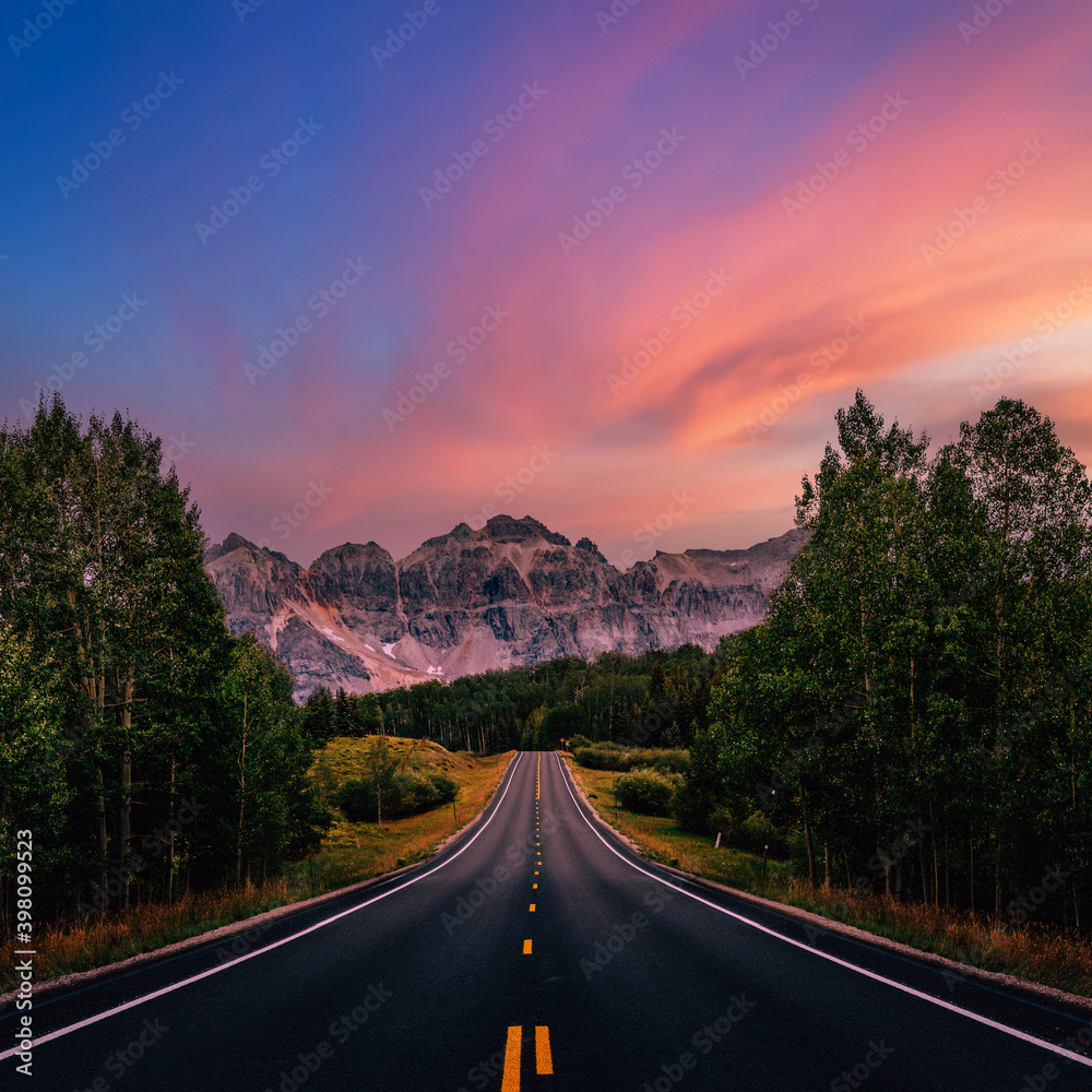 A long straight road leading towards mountains, Colorado, USA.  Road trip, traveling vibes, freedom, courage. Amazing sunset sky, dreamy landscape