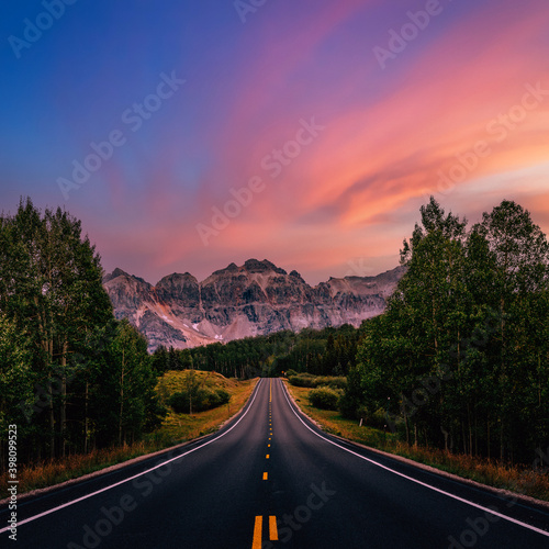 A long straight road leading towards mountains, Colorado, USA. Road trip, traveling vibes, freedom, courage. Amazing sunset sky, dreamy landscape
