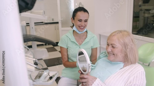 Happy senior woman smiling to the mirror at the dental clinic