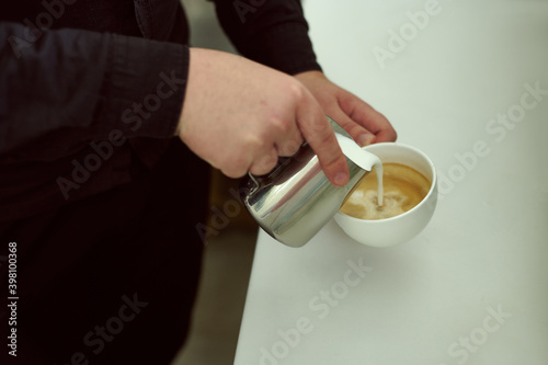 Close-up of barista holding a cup of coffe and puttig milk on