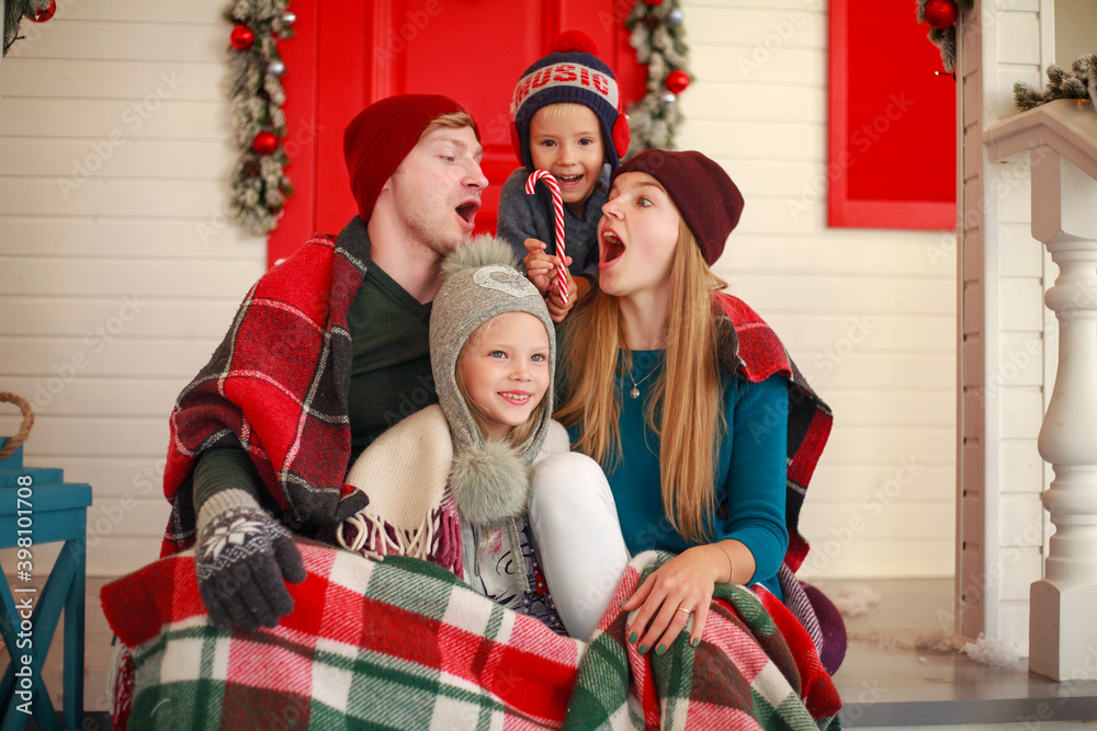 Fototapeta premium Young family with children at Christmas celebrates the new year together on porch of their house in winter