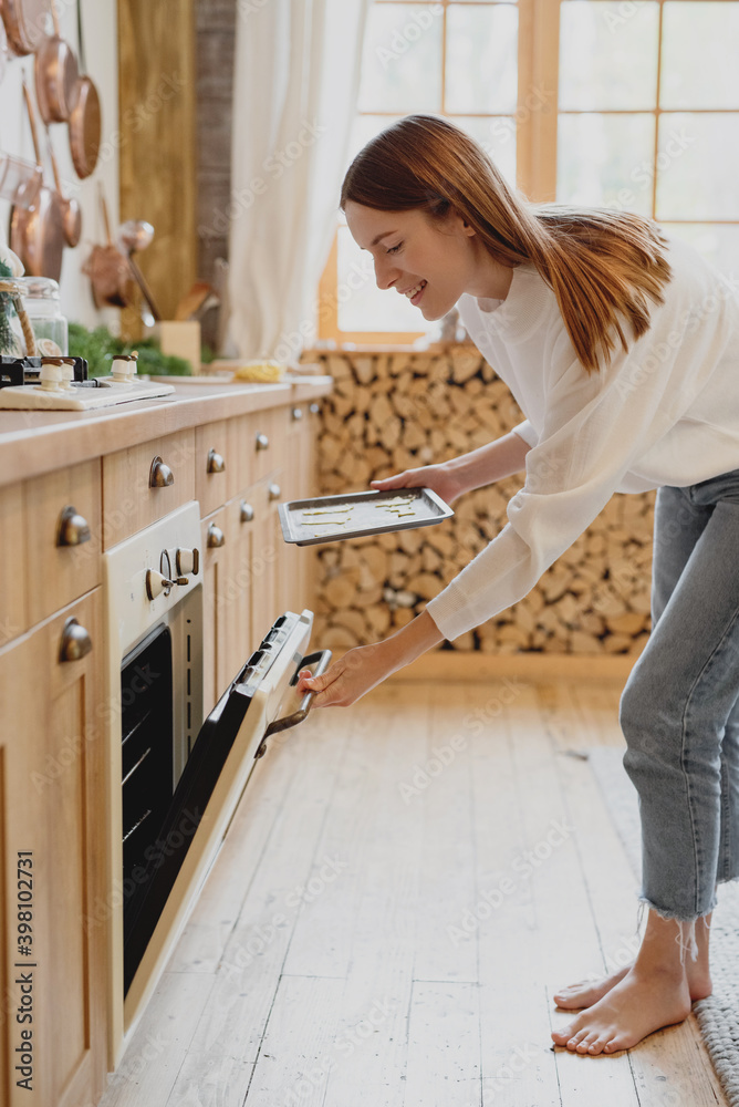 Young smiling woman placing tray with cookies in oven. Young smiling woman placing tray with cookies in oven.