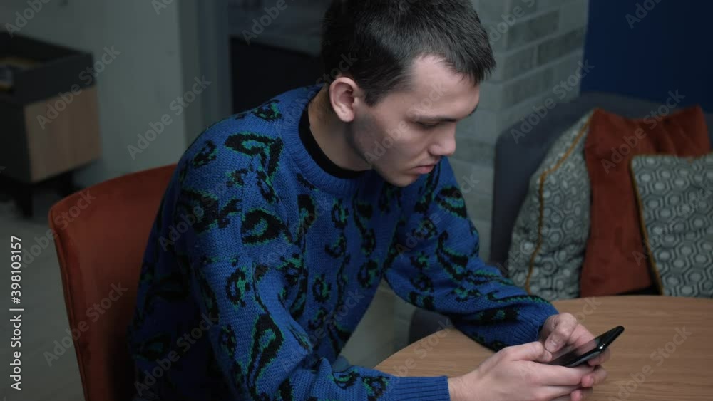Young handsome caucasian Man Uses Smartphone at Home. Man Browses Through Internet, Watches Videos and Uses Social Networks at Home.