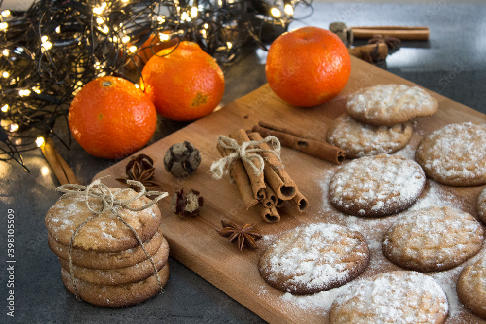 Christmas biscuits with festive decoration. Top view photo of homemade cookies, Christmas lights, tangerines, star anise and cinnamon sticks. 

