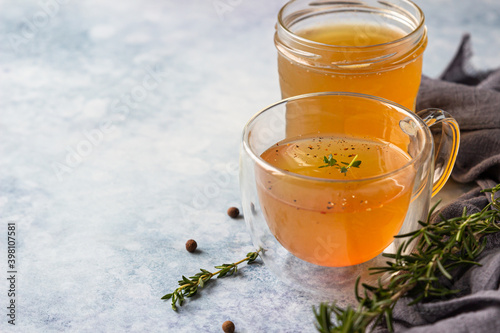 Bone or vegetable broth, bouillon in a glass mug and aromatic herbs on blue stone background. Paleo diet.