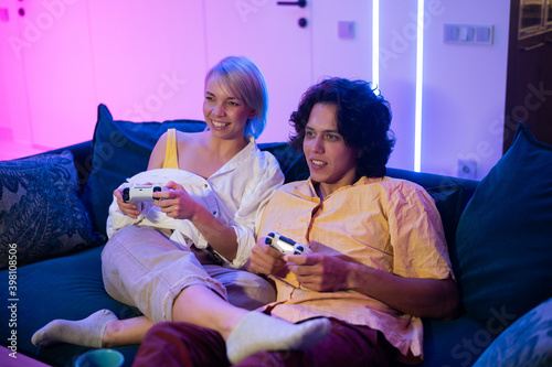 Handsome young man teaching how to play the video games to his girlfriend, on the couch, concept about home entertainment, video games. photo