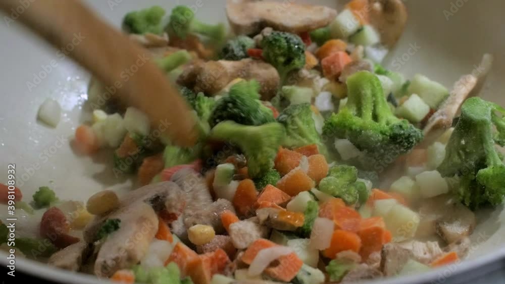 Cooking and mixing frozen vegetables in a white frying pan, making healthy vegetarian food, steam coming up, closeup handheld shot Cooking and mixing frozen vegetables in a white frying pan, making healthy vegetarian food, steam coming up, closeup handheld shot