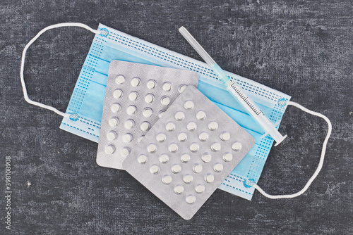 Pills, medical face mask, syringe on a gray background, top view. First aid, care during illness.