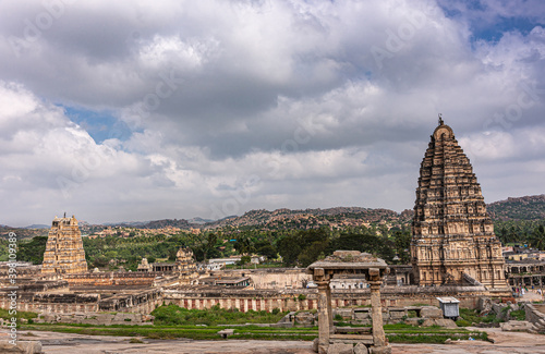 Hampi  Karnataka  India - November 4  2013  Virupaksha Temple complex. Wide landscape showing entire brown stone complex in ruins with Vimanam and Gopuram under gray cloudscape.
