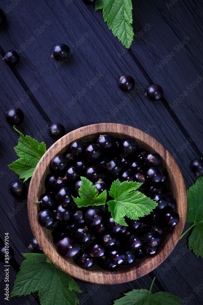 Black currant and green leaves on a dark wooden background. Background with currant berries and green leaves. Currant Macro