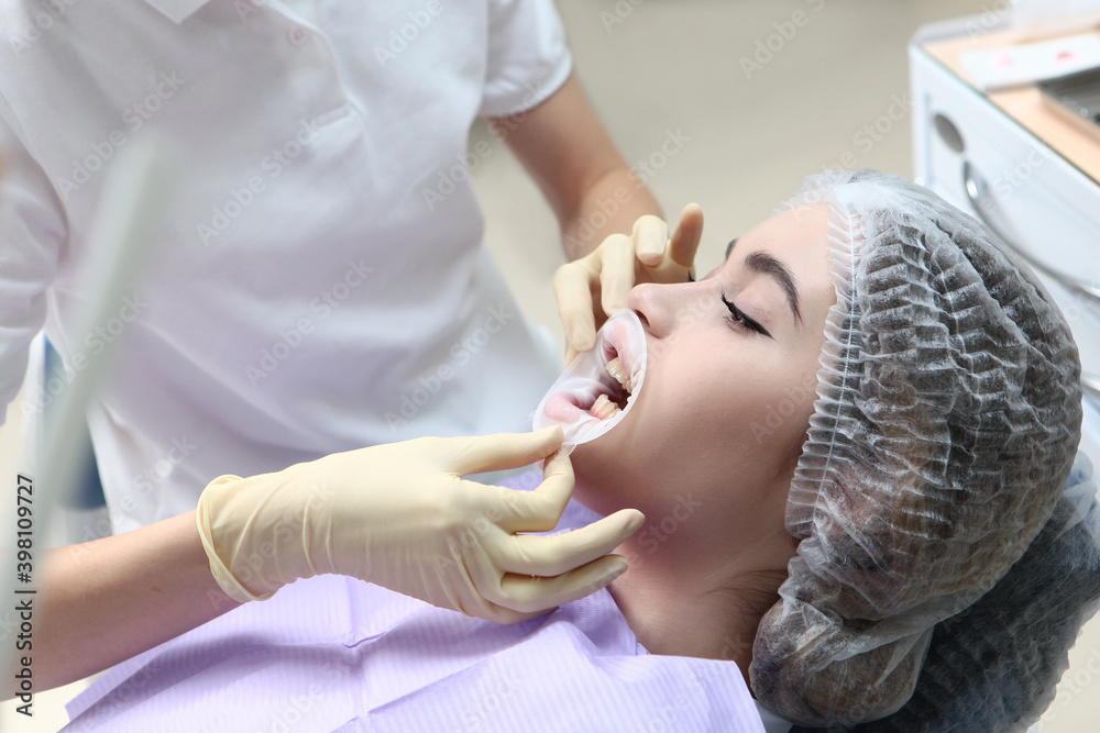 A young girl at a dentist appointment. The doctor inserts the retractor into the patient's open mouth. Concept of health protection. Prevention of caries and gum diseases. A young girl at a dentist appointment. The doctor inserts the retractor into the patient's open mouth. Concept of health protection. Prevention of caries and gum diseases.