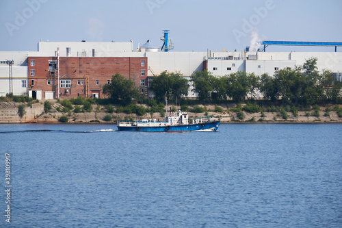 industrial landscape with a factory on the banks of the river, along which a motorship floats photo