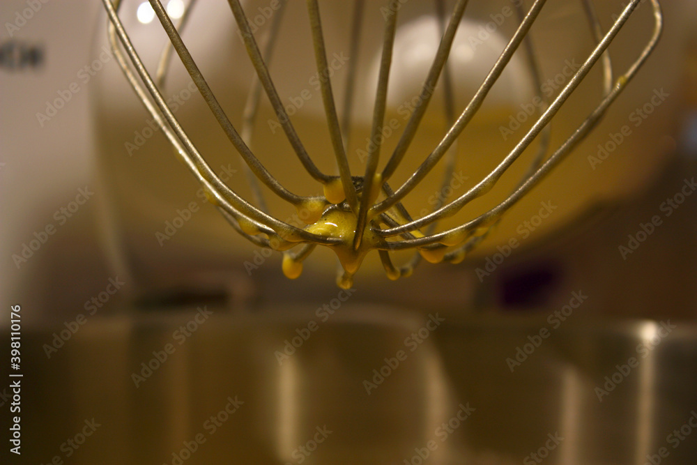 Kitchen mixer metal whisk with a raw yellow dough. Stainless steel bowl. Preparing sweet dishes like pancakes, pies, cakes, cupcakes, sweet rolls, strudels.