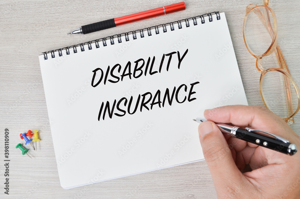 Top view of glasses, pen, pinboards and man hand holding pen writing with text DISABILITY INSURANCE. Health concept. 