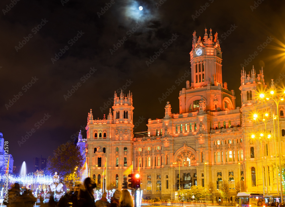 Madrid, Spain, November 28, 2020: The city of Madrid, the post office palace illuminated with red lights for Christmas, and to one side, the fountain of the Goddess Cybeles