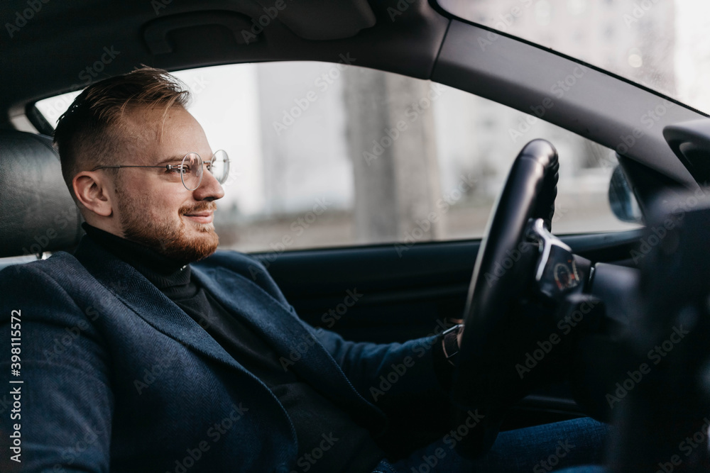 male driver in business clothes and glasses drives a car in winter.