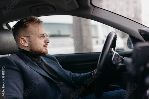 male driver in business clothes and glasses drives a car in winter. © velimir