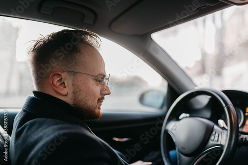 male driver in business clothes and glasses drives a car in winter.