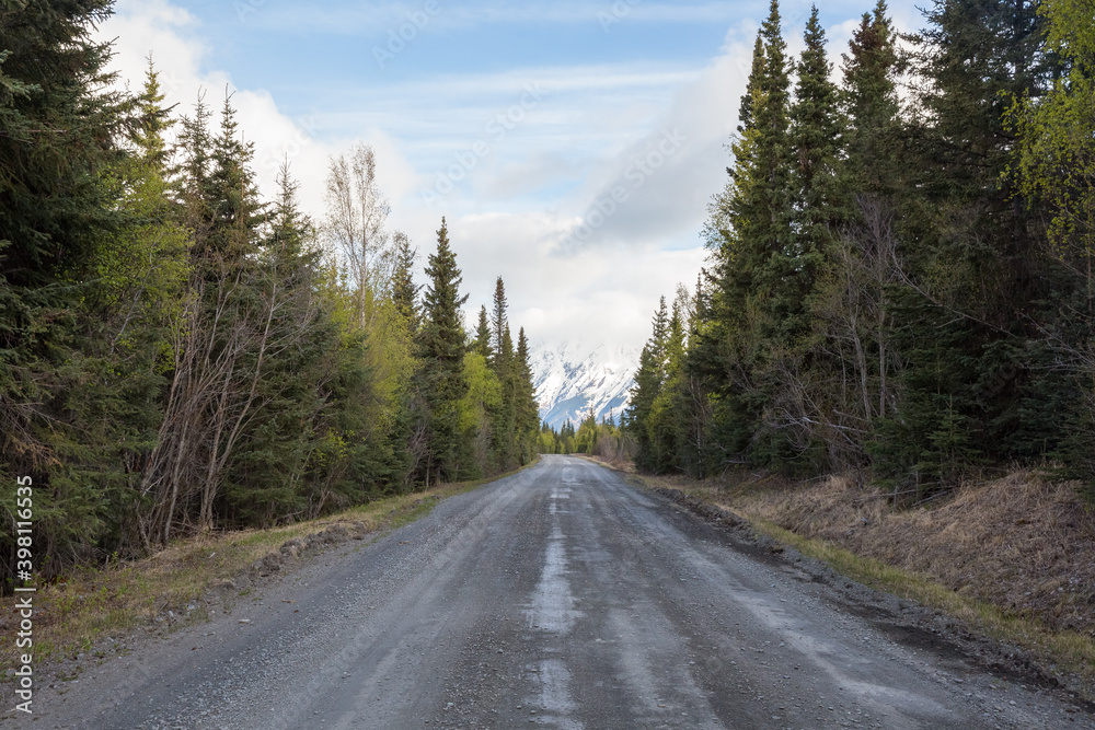 road in forest with snowy mountains and clouds in distance. Autumn afternoon in Alaska