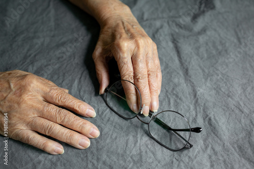 Hands of an elderly lady and glasses on a gray faded tablecloth. Aging concept