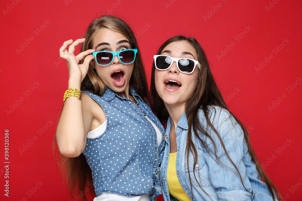 Young happy girlfriends in sunglasses on red background