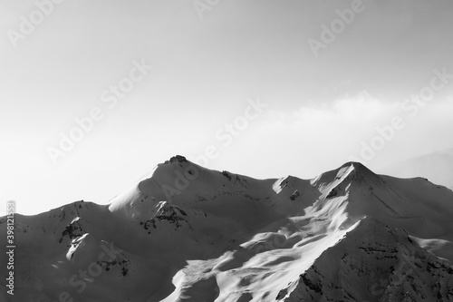 Black and white view on snowy sunlight mountains in early fog morning