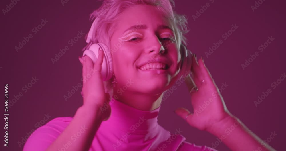 Portrait of active young woman with unusual appearance, listening music in headphones, dancing, feeling excited, moving body energetically. Pink neon light background. Portrait of active young woman with unusual appearance, listening music in headphones, dancing, feeling excited, moving body energetically. Pink neon light background.