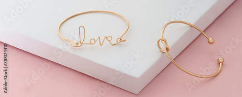 Fotografia Word love and knot shape golden bracelets on pink and white background