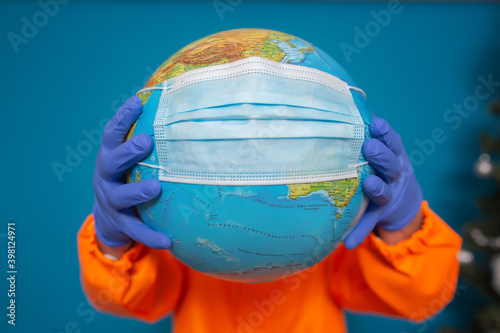 World globe with a medical mask. The hands of man in the medical gloves holding the globe isolated on blue background. Pandemic coronavirus 2019 concept.