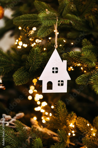 Vertical atmospheric photo Christmas decoration with a house figure on a Christmas tree with lights and balls. White House. Purchase of real estate, housing.