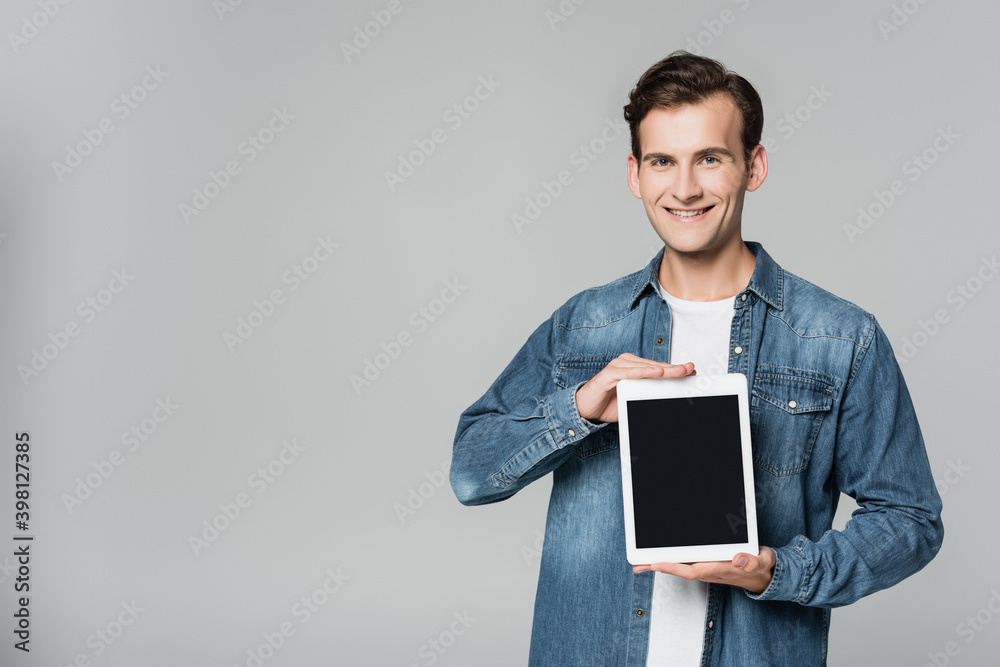 Positive man showing digital tablet with blank screen isolated on grey
