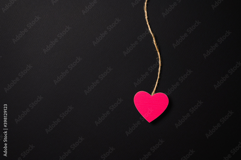 Pink small heart on a string on a dark background. There is a free empty space. Valentine's day greeting concept