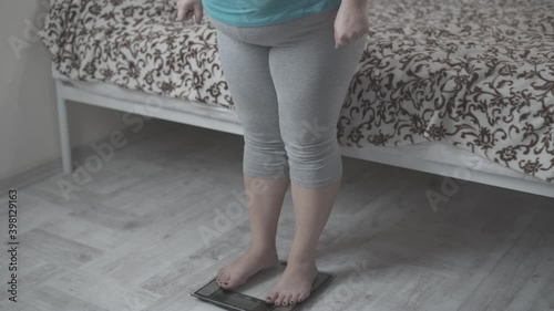 A fat woman weighs herself, looks to scale and is very happy about the good result.