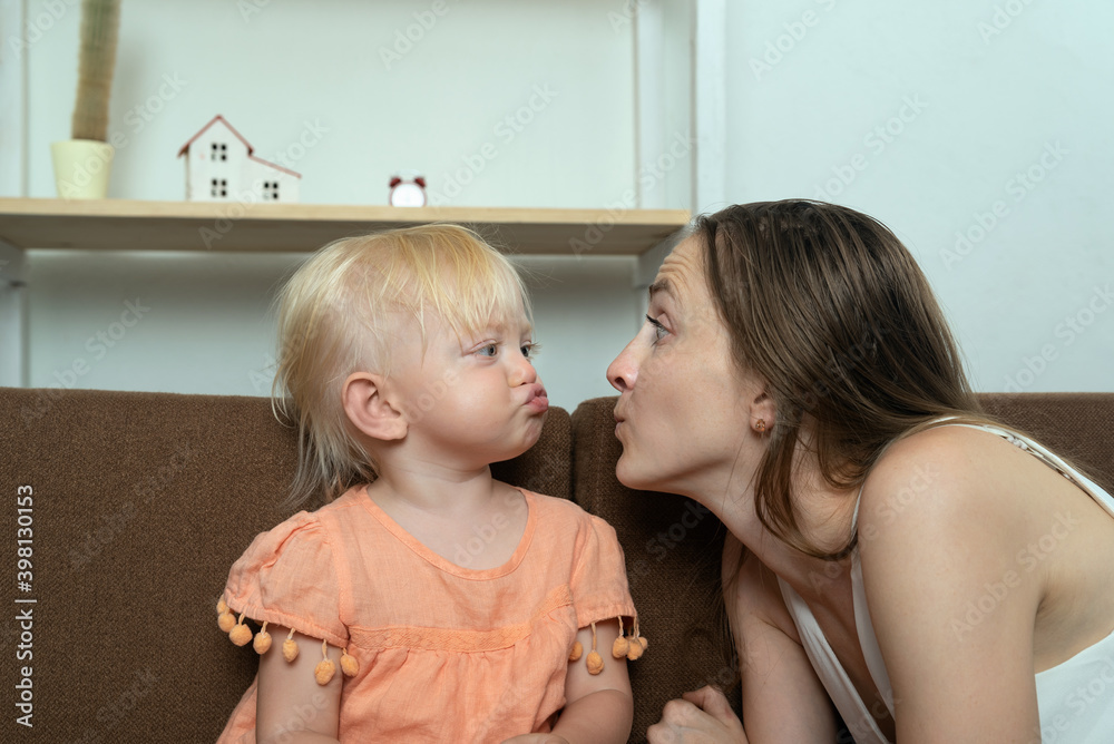 Fototapeta premium Young mom and her daughter are fun. Mom grimaces at her little daughter