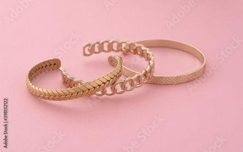 Three modern golden bracelets layed on pink background