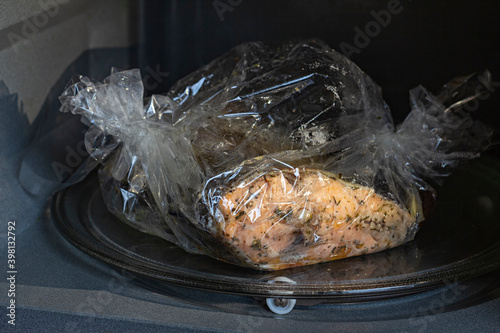Spiced fresh trout fish wrapped in a baking sleeve in a microvawe oven, cooked, closeup view photo