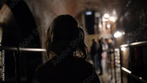 Young Girl Walking in Scary Underground Ancient Tunnel with Brick Walls photo