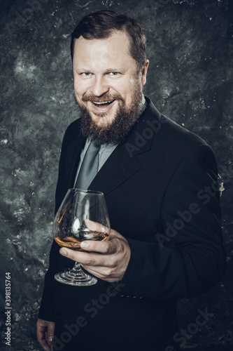 Solid smiling bearded man in suit with glass of whisky