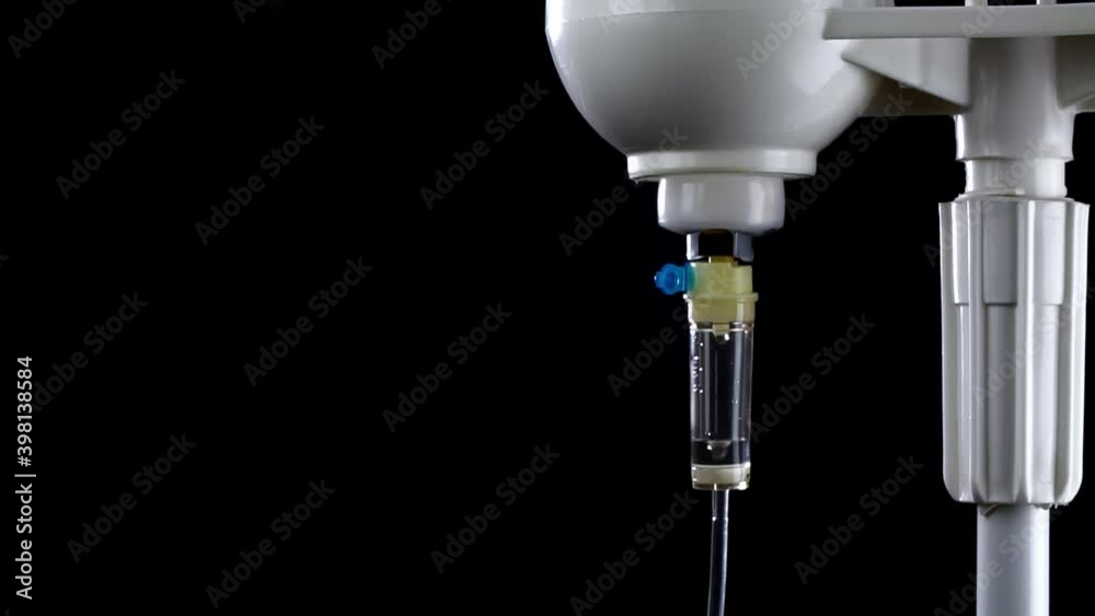 Close-up of an infusion system with falling drops on the black background in slowmo. Injection bottle with liquid drug is illuminated by blue and red emergency flashing lights. Concept of healthcare. Close-up of an infusion system with falling drops on the black background in slowmo. Injection bottle with liquid drug is illuminated by blue and red emergency flashing lights. Concept of healthcare.