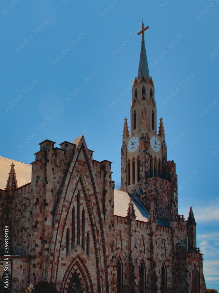 portrait image of the side view of the stone cathedral, with its tower highlighted under a cloudless blue sky.