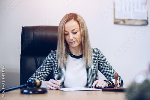 A female notary public sits at a wooden desk in her notary office signs documents.