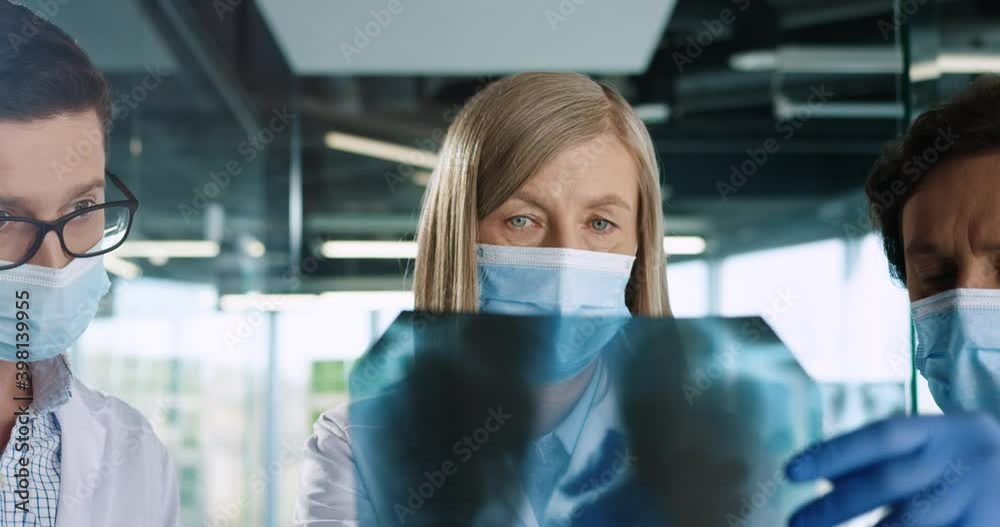 Close up of Caucasian male and female doctors coworkers in medical masks talking and discussing lungs infection looking at X-ray scan in hospital office. Team of specialists work during covid19 Close up of Caucasian male and female doctors coworkers in medical masks talking and discussing lungs infection looking at X-ray scan in hospital office. Team of specialists work during covid19