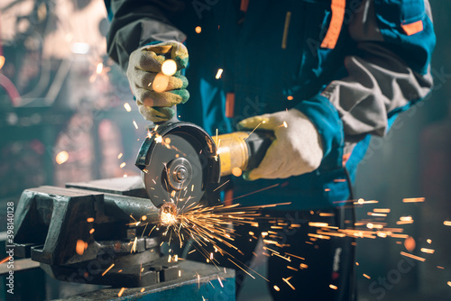 Locksmith in special clothes and goggles works in production. Metal processing with angle grinder. Sparks in metalworking