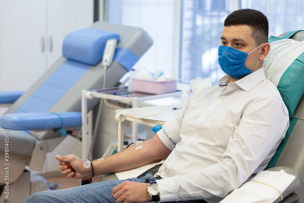 Obraz premium portrait of young man donor in medical mask from coronavirus donation blood in laboratory. prevention of covid-19 in hemodialysis transfusion unit in hospital.
