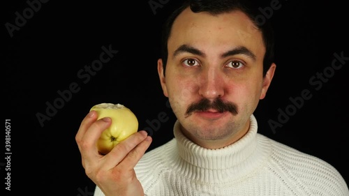 Man with mustache eating healthful green apple over black background