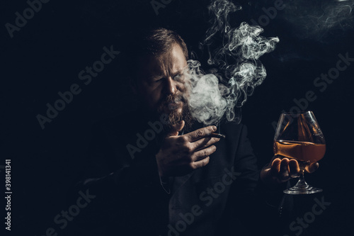 Solid confident bearded man in suit with glass of whisky and cigar with fume