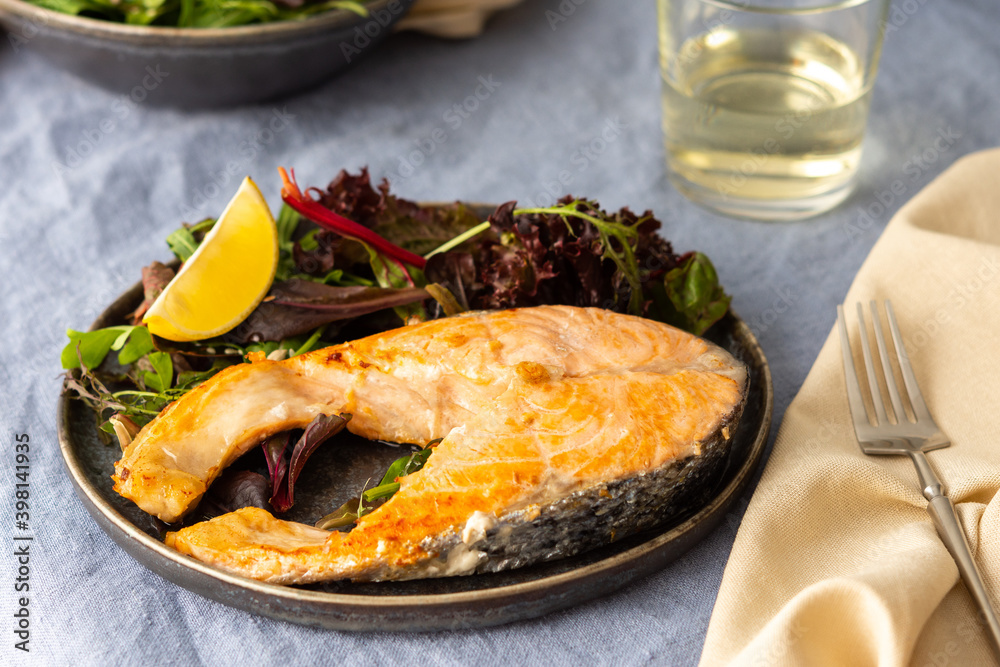 Fried salmon steak with salad in a plate close-up, white wine in a glass, delicious hearty dinner or lunch