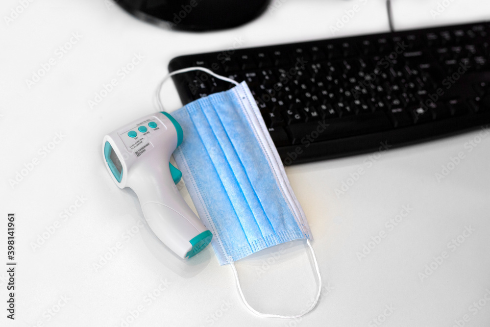 Non-contact thermometer and medical mask on a keyboard background in the office Non-contact thermometer and medical mask on a keyboard background in the office