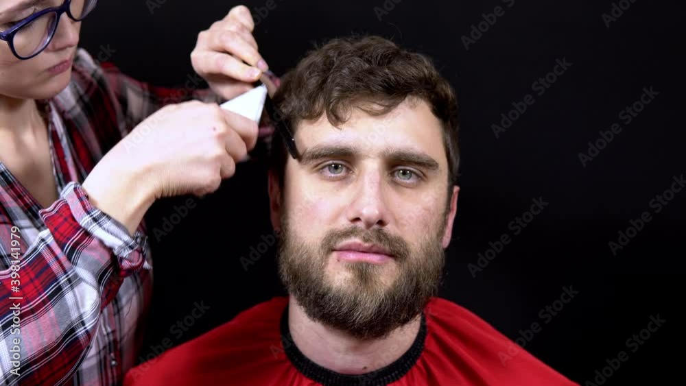 A man in a hairdressing salon a woman master cuts her hair on a black background
